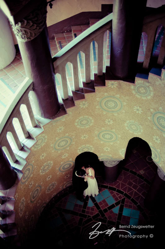 Couple standing close together below the spiral staircase at the Santa Barbara Courthouse.