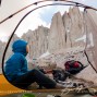 Climber in front of tent with big granite spires behind.