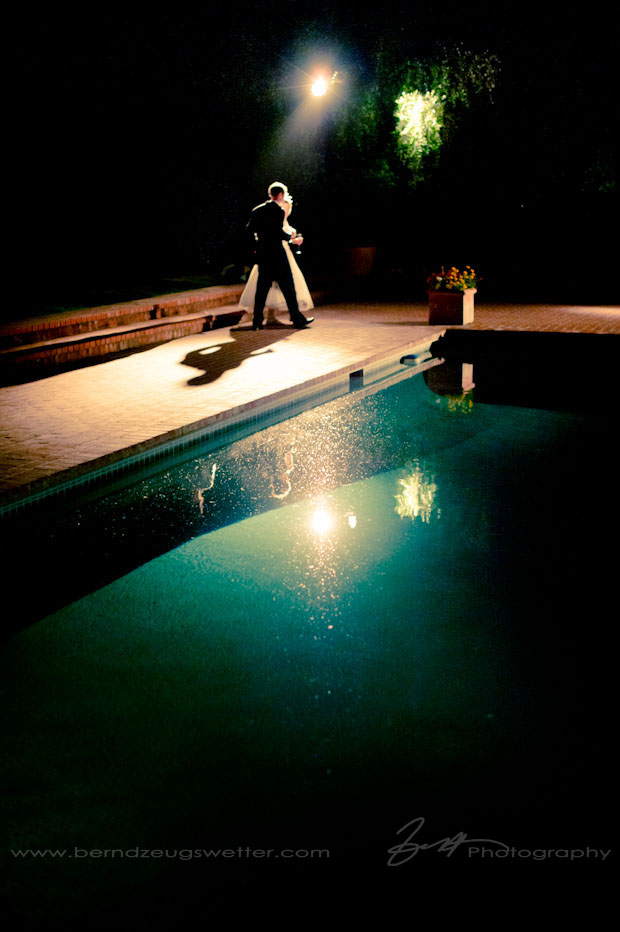 Wedding couple walking at night next to pool.