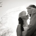 Portrait of bride and groom under blowing veil.